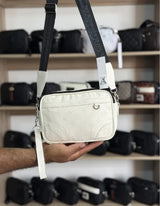 Bolso cruzado blanco texturizado con correa negra estampada y etiqueta colgante